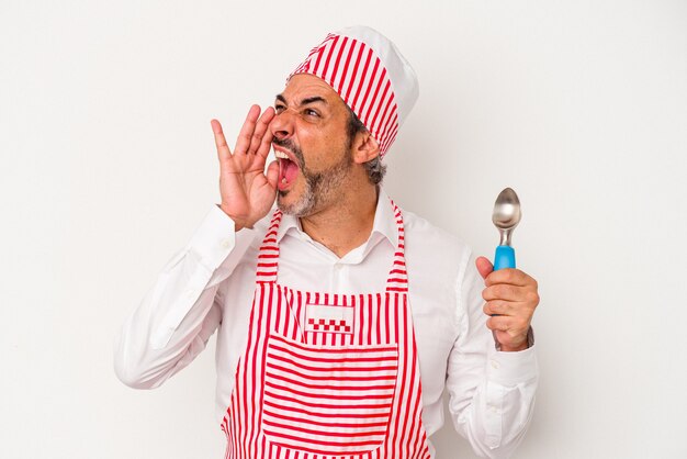 Middle age caucasian ice maker caucasian man holding a spoon isolated on white background  shouting and holding palm near opened mouth.