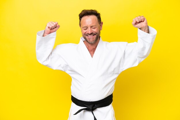 Photo middle age caucasian man doing karate isolated on yellow background doing strong gesture