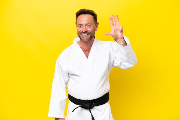 Middle age caucasian man doing karate isolated on yellow background happy and counting four with fingers