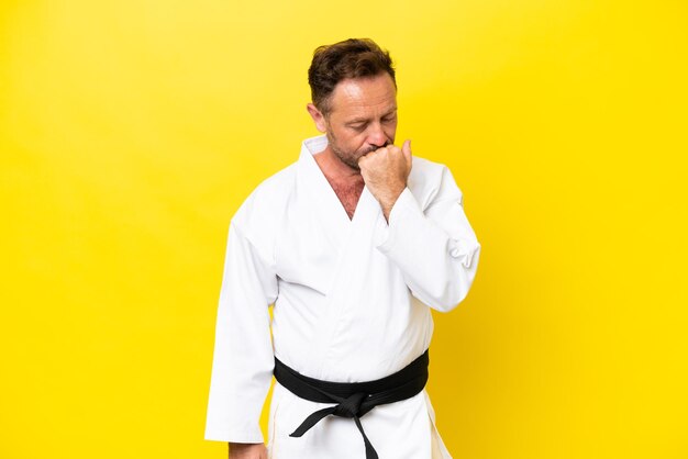 Foto uomo caucasico di mezza età che fa karate isolato su sfondo giallo con dubbi