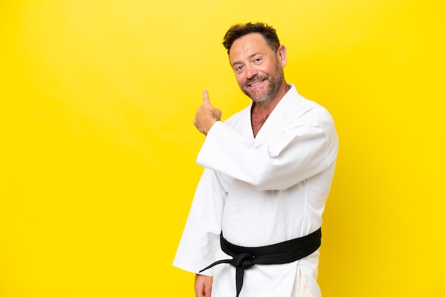 Middle age caucasian man doing karate isolated on yellow background pointing back