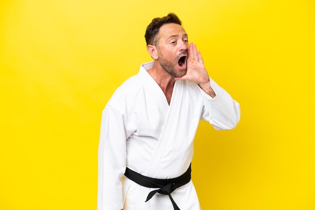 Foto uomo caucasico di mezza età che fa karate isolato su sfondo giallo che grida con la bocca spalancata di lato