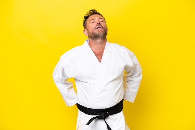 Photo middle age caucasian man doing karate isolated on yellow background suffering from backache for having made an effort