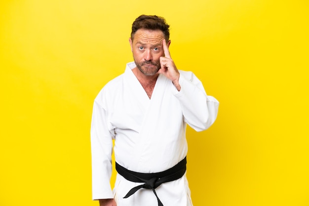 Foto uomo caucasico di mezza età che fa karate isolato su sfondo giallo pensando un'idea