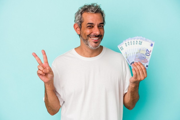 파란색 배경에 격리된 지폐를 들고 있는 중년 백인 남자는 손가락으로 평화의 상징을 보여주는 즐겁고 평온하다