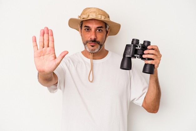 Middle age caucasian man holding binoculars isolated on white background standing with outstretched hand showing stop sign preventing you