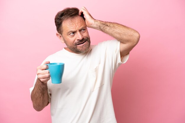 Middle age caucasian man holding cup of coffee isolated on pink background having doubts and with confuse face expression