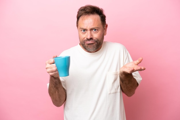 Белый мужчина средних лет держит чашку кофе на розовом фоне, делая жест сомнений, поднимая плечи
