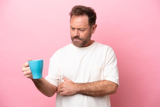 Middle age caucasian man holding cup of coffee isolated on pink background with sad expression