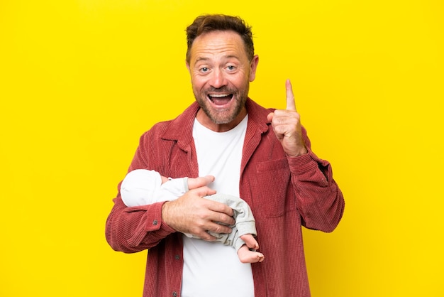 Middle age caucasian man holding his newborn son isolated on yellow background pointing up a great idea