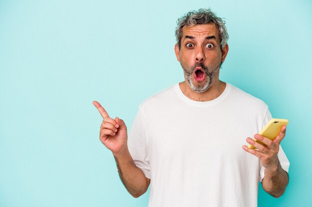 Middle age caucasian man holding a mobile phone isolated on blue background  pointing to the side