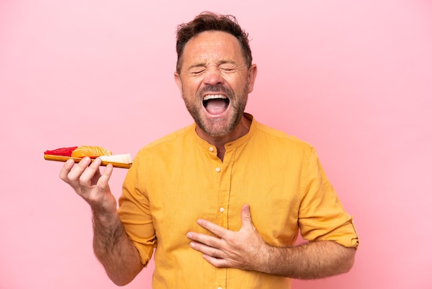 Middle age Caucasian man holding sashimi isolated on pink background smiling a lot