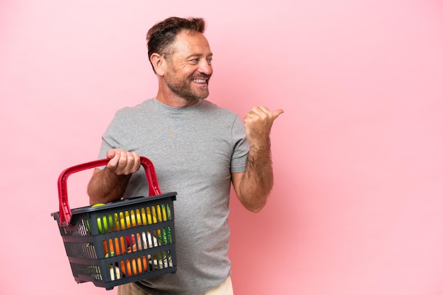 Белый мужчина средних лет держит корзину с покупками на розовом фоне