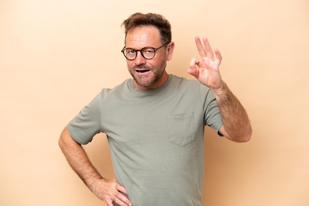 Middle age caucasian man isolated on beige background showing ok sign with fingers