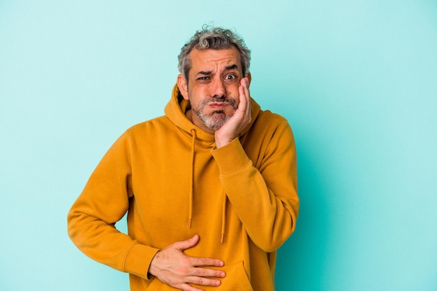 Photo middle age caucasian man isolated on blue background  blows cheeks, has tired expression. facial expression concept.