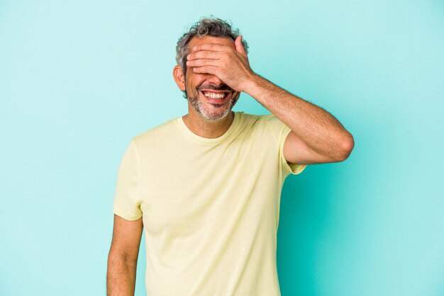 Middle age caucasian man isolated on blue background  covers eyes with hands, smiles broadly waiting for a surprise.