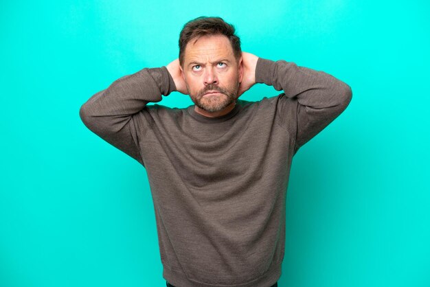 Middle age caucasian man isolated on blue background frustrated and covering ears