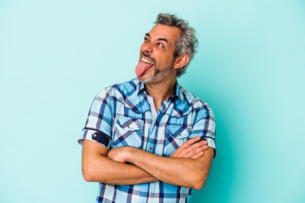 Foto uomo caucasico di mezza età isolato su sfondo blu divertente e amichevole che attacca fuori la lingua.