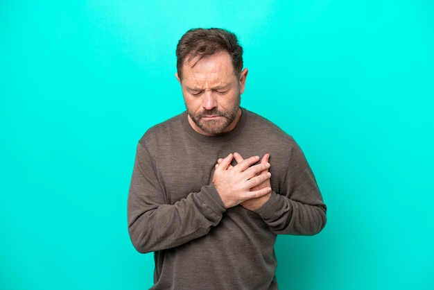 Middle age caucasian man isolated on blue background having a pain in the heart