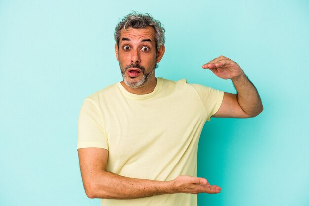 Middle age caucasian man isolated on blue background  holding something with both hands, product presentation.