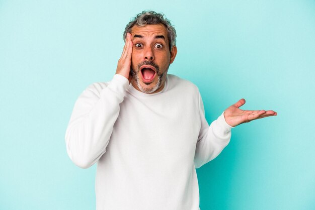 Photo middle age caucasian man isolated on blue background  impressed holding copy space on palm.