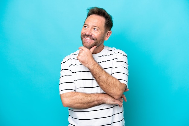 Middle age caucasian man isolated on blue background looking up while smiling