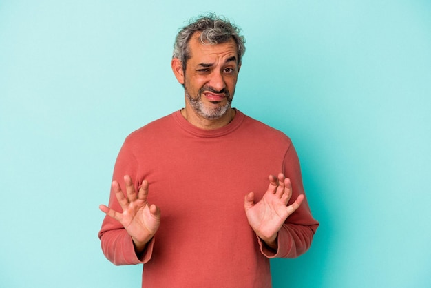 Middle age caucasian man isolated on blue background  rejecting someone showing a gesture of disgust.