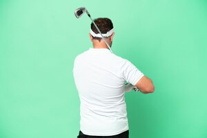 Middle age caucasian man isolated on green background playing golf