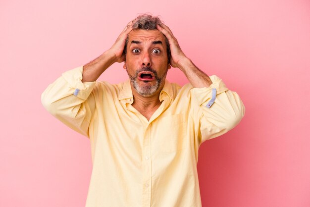 Middle age caucasian man isolated on pink background being shocked she has remembered important meeting