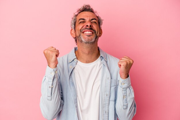 Uomo caucasico di mezza età isolato su sfondo rosa che celebra una vittoria, passione ed entusiasmo, espressione felice.