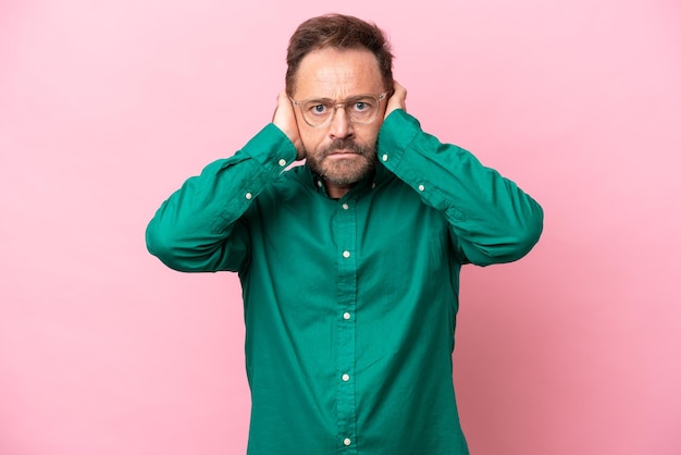 Middle age caucasian man isolated on pink background frustrated and covering ears