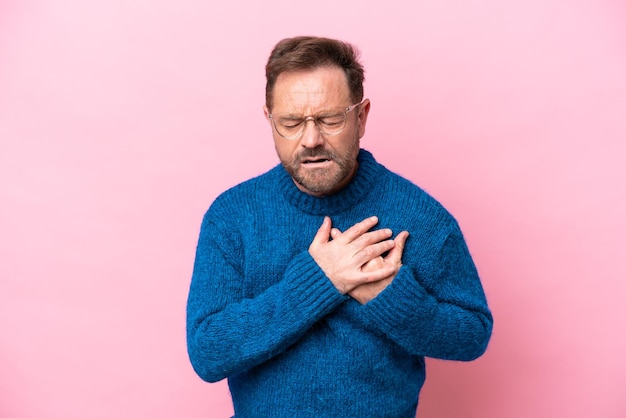 Middle age caucasian man isolated on pink background having a pain in the heart