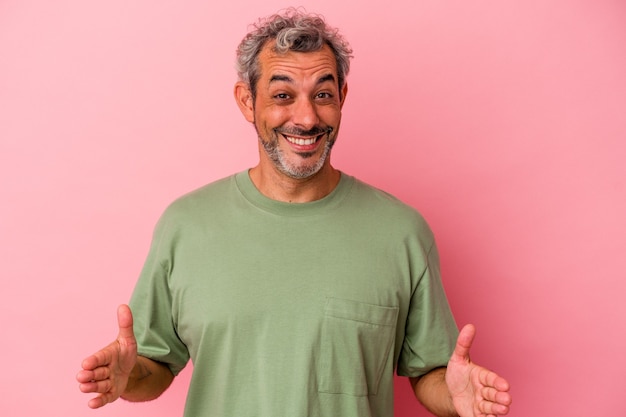 Middle age caucasian man isolated on pink background  holding something with both hands, product presentation.