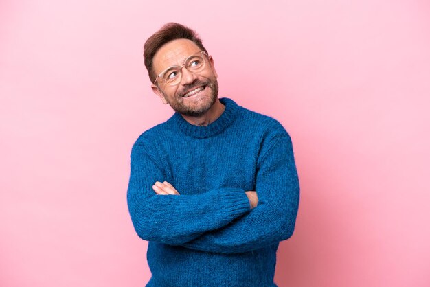 Middle age caucasian man isolated on pink background looking up while smiling