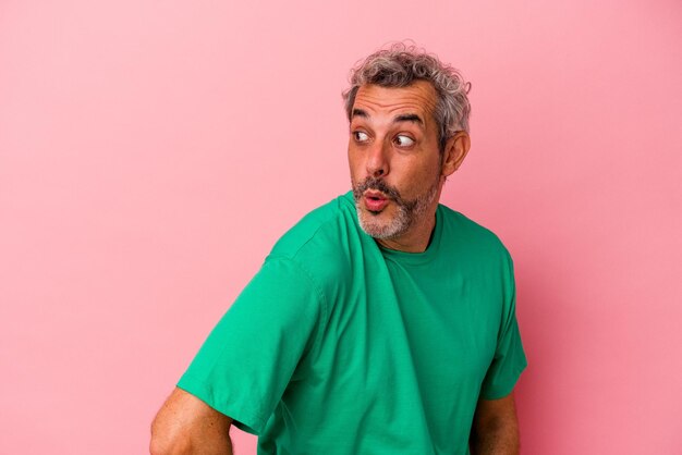 Middle age caucasian man isolated on pink background  looks aside smiling, cheerful and pleasant.