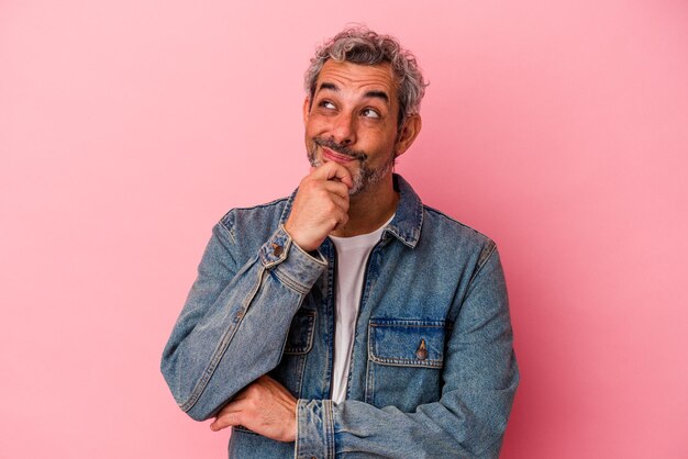 Middle age caucasian man isolated on pink background relaxed thinking about something looking at a copy space