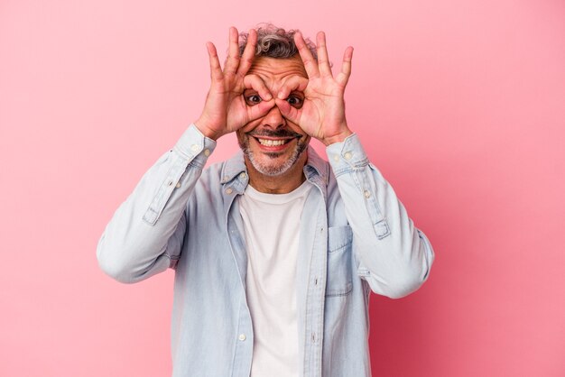 Middle age caucasian man isolated on pink background  showing okay sign over eyes