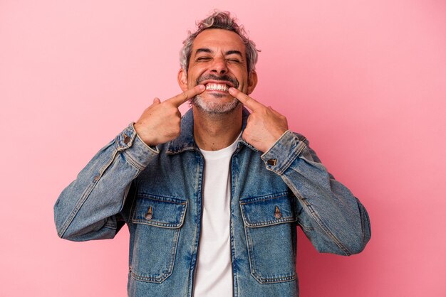 Middle age caucasian man isolated on pink background smiles pointing fingers at mouth