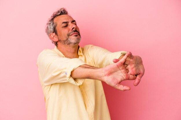 Middle age caucasian man isolated on pink background stretching arms relaxed position