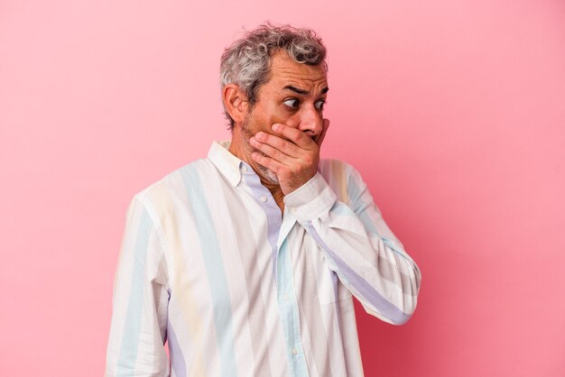 Photo middle age caucasian man isolated on pink background  thoughtful looking to a copy space covering mouth with hand.