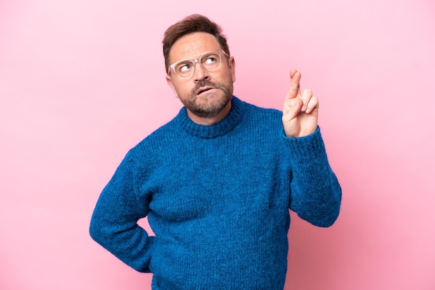 Middle age caucasian man isolated on pink background with fingers crossing and wishing the best
