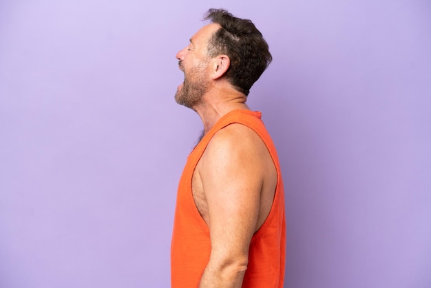 Middle age caucasian man isolated on purple background laughing in lateral position