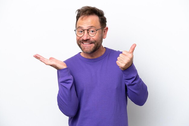 Middle age caucasian man isolated on white background holding copyspace imaginary on the palm to insert an ad and with thumbs up