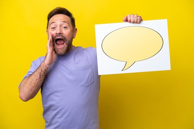 Middle age caucasian man isolated on yellow background holding a placard with speech bubble icon and shouting