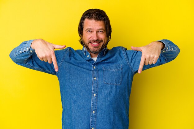 Middle age caucasian man isolated on yellow background points down with fingers, positive feeling.