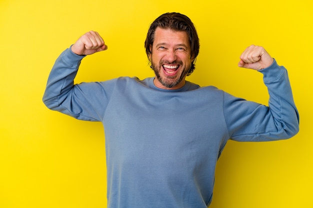 Middle age caucasian man isolated on yellow background showing strength gesture with arms, symbol of feminine power