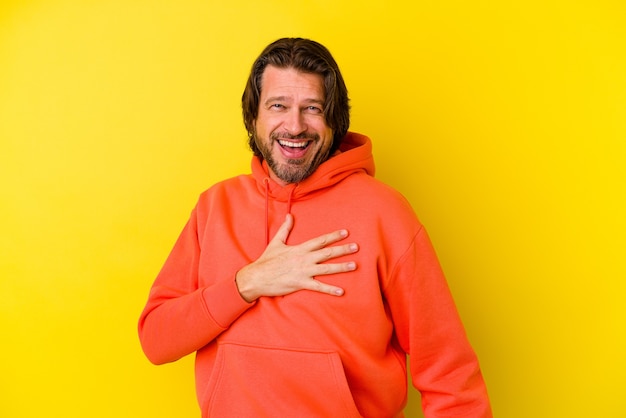 Middle age caucasian man isolated on yellow wall laughs out loudly keeping hand on chest