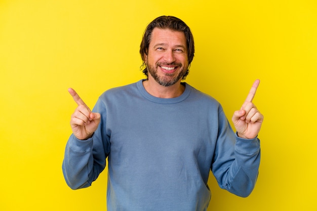 Middle age caucasian man isolated on yellow wall pointing to different copy spaces, choosing one of them, showing with finger.