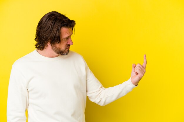 Middle age caucasian man isolated on yellow wall pointing with finger at you as if inviting come closer