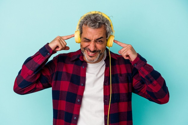 手で耳を覆う青い背景で隔離の音楽を聴いている中年白人男性